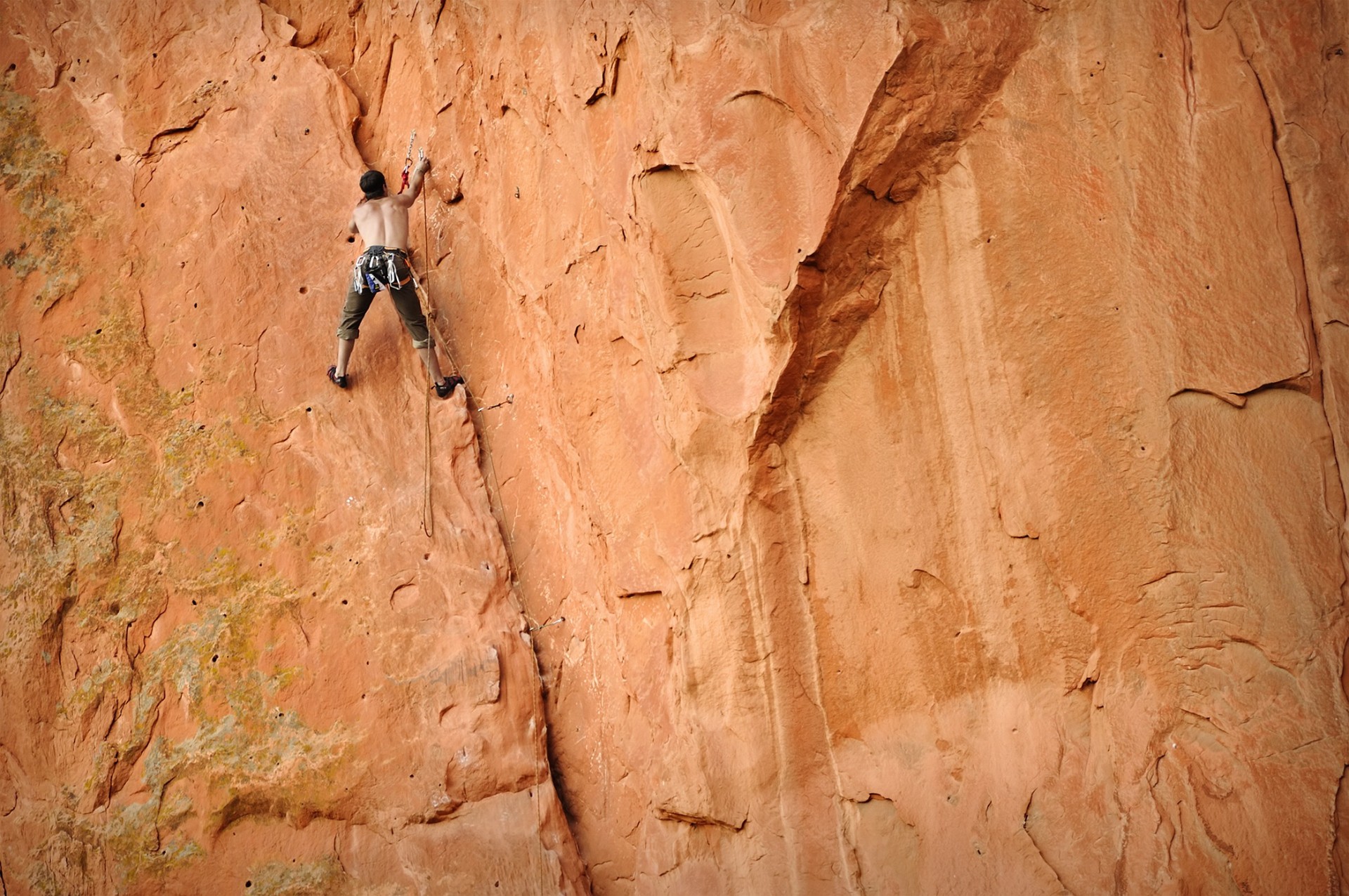 Rock climber ascending a tall red sandstone wall on a rope in Colorado's Red Rock Country