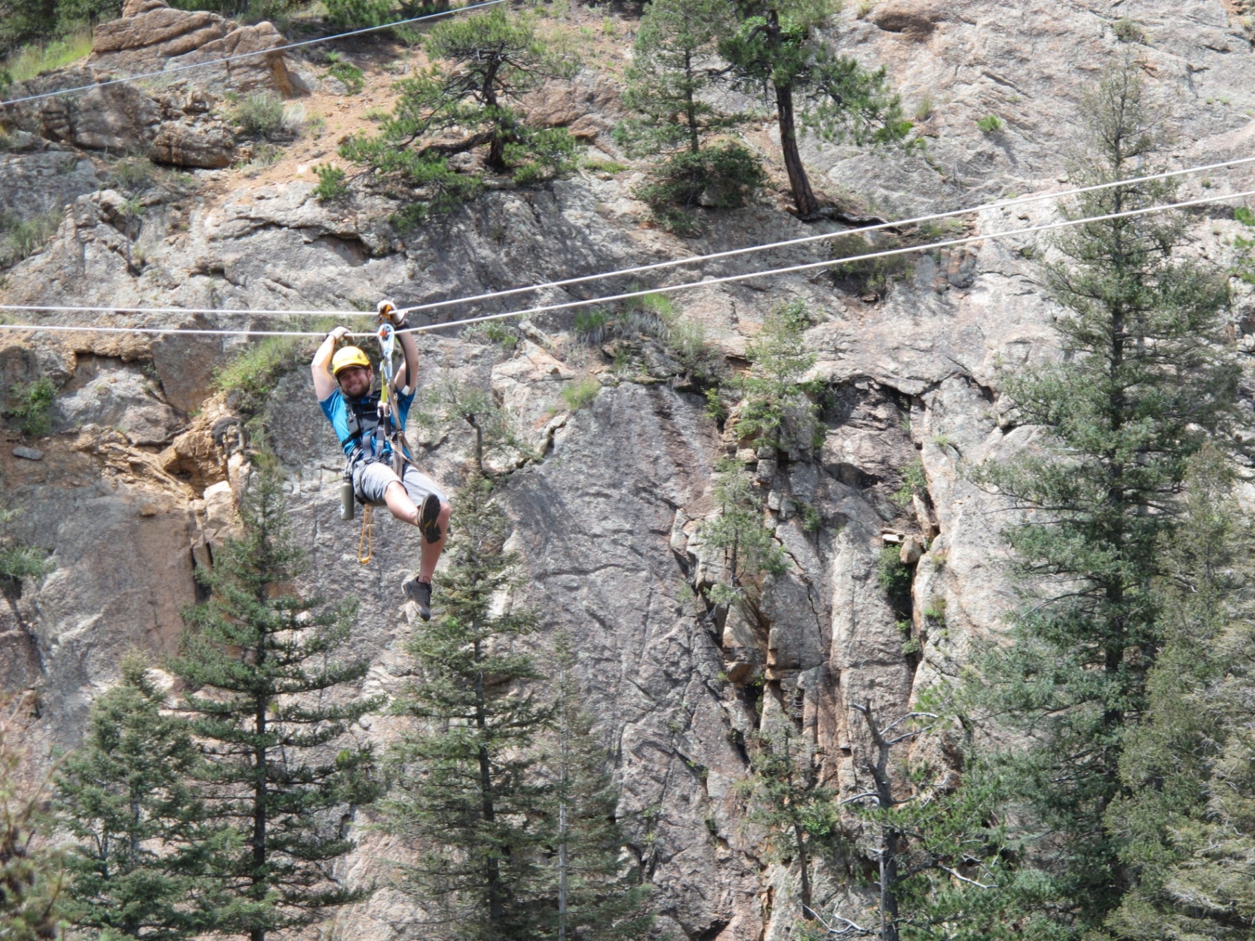 Guest ziplining across a granite canyon lined with pine trees at Seven Falls in Colorado Springs